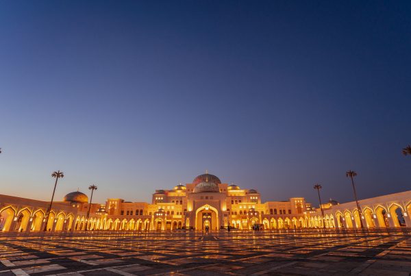 An exterior landscape shot of Qasr Al Watan Palace during the evening as the Palace is illuminated by bright yellow lights.